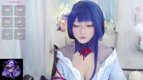 Media: Video of a young Asian woman with blue hair in a cosplay outfit, featuring a low-cut white blouse revealing ample cleavage. Background includes stuffed animals and a white curtain.