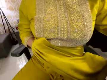 Media: Video of a person wearing a bright yellow, intricately embroidered shirt with golden floral patterns and a matching pair of yellow pants, seated in a modern office chair. The background features a white and black tiled floor and a black desk with a black laptop.