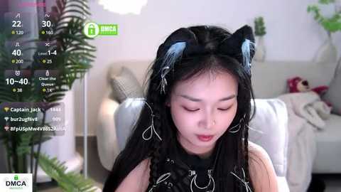 Media: Video of an East Asian woman with long black hair, wearing cat ears, and black clothes, sitting on a white couch, with live streaming overlay.