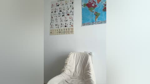 Media: A video of a minimalist white-walled room featuring a cream-colored beanbag chair, a colorful alphabet poster, and a world map poster.