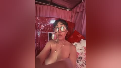 Media: A video of a topless woman with short black hair, wearing glasses, blowing a kiss. She's in a pink room with a red bed and a teddy bear.