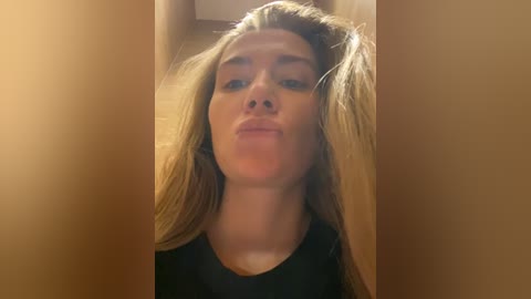 A video of a young woman with long blonde hair, blowing a kiss, taken from a low angle through a narrow opening, creating a playful, intimate, and slightly voyeuristic effect.