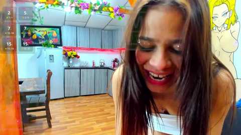 Media: Video of a smiling, dark-haired woman in a modern, colorful kitchen with wooden floors, cabinets, and floral decorations.