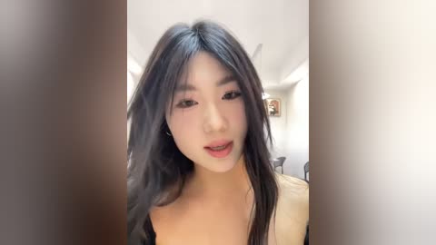 Media: Video of an East Asian woman with long black hair, fair skin, and delicate features, smiling in a modern, minimalist room with white walls and ceiling lights.