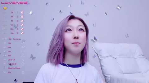 Media: A video of a young Asian woman with shoulder-length, pastel pink hair, wearing a white T-shirt, against a soft, silver confetti backdrop.