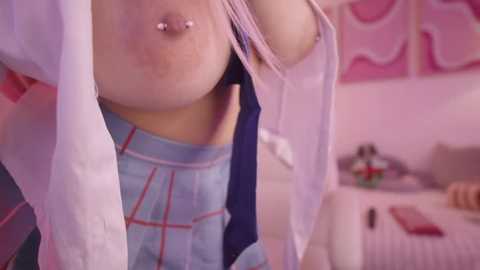 Media: Video of a young woman with a pierced nipple, partially undressing in a pink room with a bed and toy car.