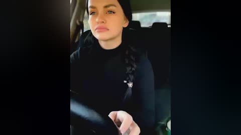 Media: A video of a young woman with fair skin, long black hair, and light makeup, wearing a black sweater, sitting in a car.