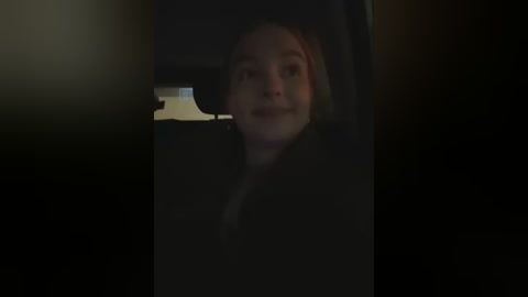 Media: A dimly-lit video shows a young woman with fair skin and light brown hair, slightly blurry, looking out a car window, with dark, shadowy surroundings.