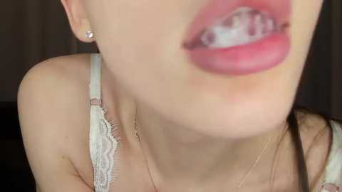 Video of a close-up of a young woman with fair skin, wearing a light-colored lace bra, and showing her braces.