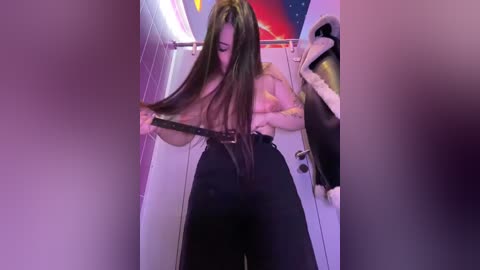 A video of a woman with long, dark hair, topless, wearing black pants, adjusting a belt in a dimly lit room with purple lighting and a Star Wars poster.