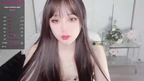 Media: Video of a young, fair-skinned woman with long, straight black hair, wearing red lipstick, a white top, and sitting in a modern room with a glass table and flowers.