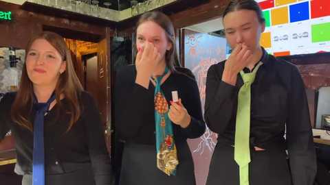 Media: Video of three young women in formal attire, wearing ties, inside a brightly lit restaurant. The background features a colorful menu board and a green exit sign.