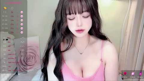 Media: A video of a young Asian woman with long black hair, wearing a pink spaghetti-strap top, posing indoors with a soft, pastel-toned background.