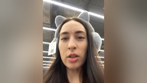 Media: Video of a young woman with long, dark hair wearing a gray, cat-ear headband, slightly blurred background of an industrial ceiling.