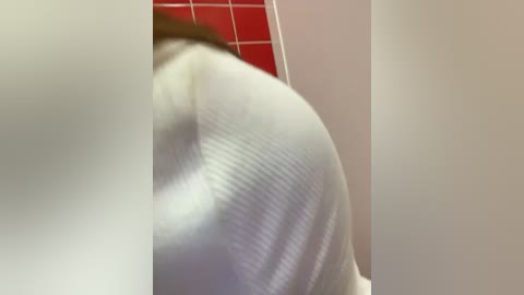 Media: A video of a person's buttocks, clad in tight, white, ribbed leggings, positioned against a red-tiled wall. The image is slightly blurred, focusing on the curves and texture of the clothing.