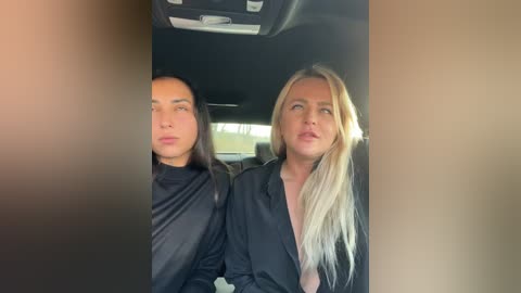 Media: Video of two women, one with long dark hair, the other with long blonde hair, sitting in a car, looking out the window, wearing black tops, blurred background.