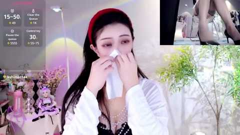 Media: Video collage featuring a young Asian woman in a red beret, white blouse, and polka-dot dress, sneezing into a tissue, surrounded by virtual maid figures in a pastel-themed room.