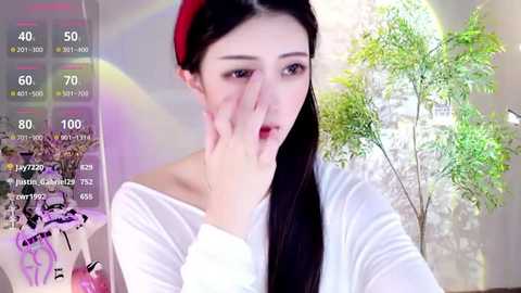 Media: A video of an East Asian woman with long black hair and a red beret, wearing a white off-shoulder top, touching her face, surrounded by virtual reality elements.