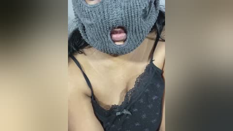 Media: Video of a woman's face, partially obscured by a dark gray knit mask, wearing a black lace-trimmed spaghetti strap top, mouth open, light skin tone.