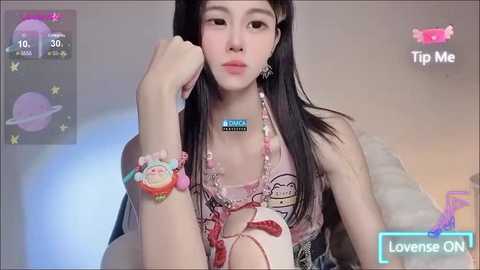 Media: A video of an Asian woman with long black hair, wearing a pink crop top and multiple bracelets, sitting on a couch, with a \"Tip Me\" overlay.