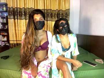 Media: Video of two South Asian women in matching black face masks, one in a floral nightgown, the other in a bra and panties, sitting on a green bed with yellow curtains.