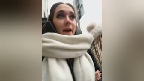 Media: Video of a distressed woman with long brown hair, wearing a white scarf and dark jacket, gripping a teddy bear tightly, looking fearful and anxious.