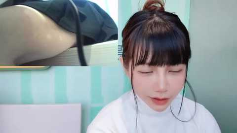 Media: Video of a young Asian woman with fair skin and dark hair in a bun, wearing a white turtleneck and headphones, in a pastel-colored bathroom with striped wallpaper.