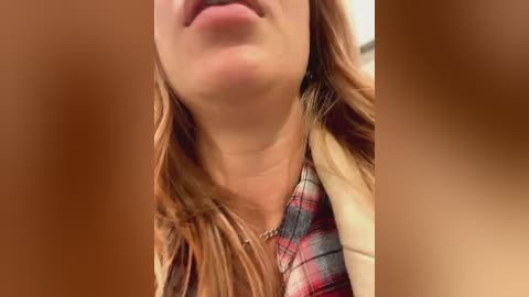 Media: Video of a close-up of a woman's upper body, focusing on her lips and neck. She has light skin and wears a red plaid shirt. The background is blurred, making the subject stand out.