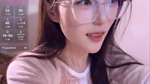 Media: Video of a fair-skinned East Asian woman with long, straight brown hair, wearing large, clear glasses and a white lace top, smiling softly. Background shows a virtual dating screen with chat and heart icons.