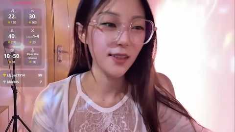 Media: Video of an East Asian woman with long black hair, wearing glasses and a white lace top, smiling slightly. Background shows a room with a wooden door and a pinkish glow.