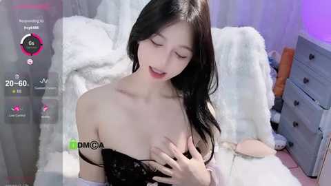 Media: A video of an Asian woman with long black hair and fair skin, lying on a white bed in a dimly lit room, wearing a black lace top.