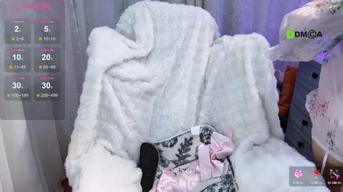 Media: Video of a plush white rabbit in a cozy, dimly lit room. The rabbit is sitting on a white fluffy blanket, with a pink and white patterned pillow nearby.