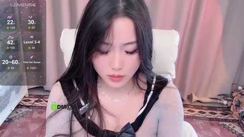 Media: A video of a young East Asian woman with long black hair, wearing a schoolgirl outfit, sitting in a chair. Background shows a room with a digital clock and a pink curtain.