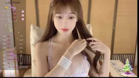 Media: A video of an East Asian woman with long brown hair, wearing a lavender lace bra, sitting in a dimly lit room with a wooden screen background. She's brushing her hair.