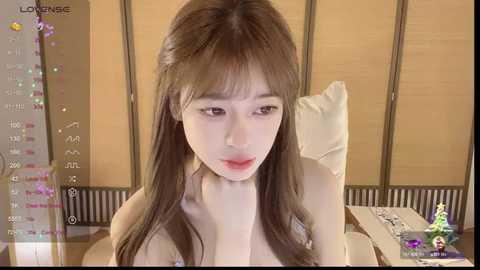 Media: Video of a young Asian woman with long brown hair, fair skin, and red lipstick, sitting at a desk in a room with light-colored walls and a wooden screen. She looks focused, possibly reading a book.