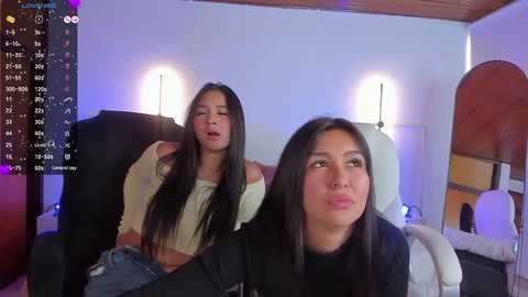 Media: Video of two young Asian women in a modern, dimly-lit living room, one asleep on a black couch, the other looking tired.