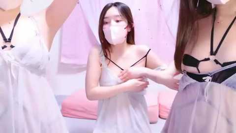 Media: Video of a young Asian woman in a white dress, kneeling, adjusting straps on a white dress held by two other women.