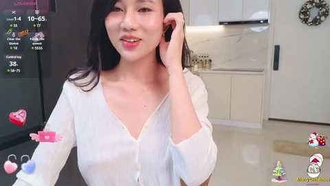 Media: Video of an Asian woman with long black hair, wearing a sheer white blouse, in a modern kitchen. She's smiling and talking on a phone.