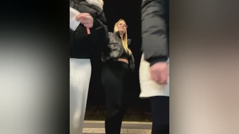 Media: Video of a blonde woman in black puffer jacket and pants, performing a kick in a dimly lit, urban setting.