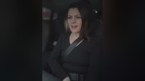 Media: A video captures a woman with shoulder-length dark hair and a black jacket, seated in a dimly lit car, possibly crying. The image is slightly out of focus.