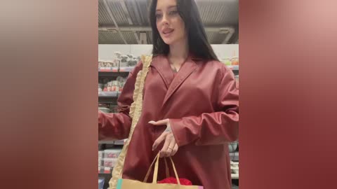 Media: Video of a young woman with long black hair, wearing a red satin blazer, shopping in a store with shelves of products in the background.