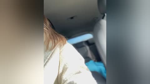 Media: A video of a woman in a light-colored sweater, seen from behind, sitting in a car with sunlight streaming through a window, creating a shadowy effect.