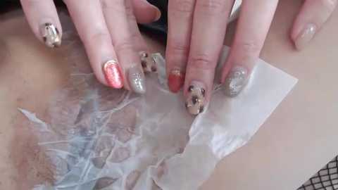 Media: Video of a close-up of a person's hands with manicured nails, featuring glittery and metallic designs, applying a clear adhesive to the skin, possibly for a temporary tattoo.