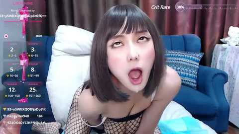 Media: A video of an East Asian woman with straight, shoulder-length black hair, wearing a fishnet top and fishnet stockings, performing oral sex on a man. The background shows a blue couch, curtains, and a table with a white cloth.