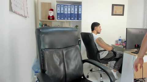 Media: Video of a modern office with a man in a white shirt and gray pants working on a computer at a desk, surrounded by blue file cabinets and a Christmas elf figurine.