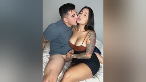 Media: Video of a Latino man and Latina woman passionately kissing on a bed, both partially nude. She wears a low-cut brown top, exposing cleavage.