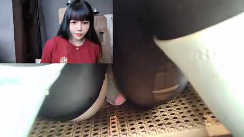 Media: Video: A young woman with black hair, wearing a red shirt, sits on a chair. A close-up of her feet shows black and white sneakers. Background includes a woven chair and a wooden door.