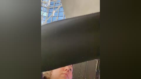 Media: Video of a person's face partially obscured by a vertical black object, possibly a pole or barrier, with a modern glass and steel structure visible in the background.