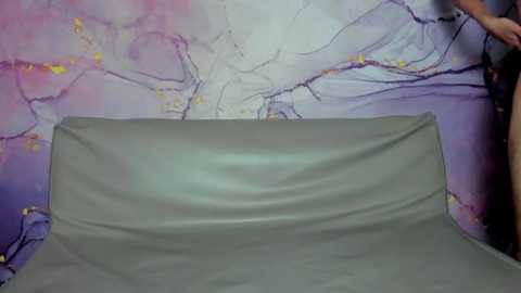 Media: Video of a grey couch in a room with a vibrant, abstract purple and pink wall adorned with delicate, swirling patterns.