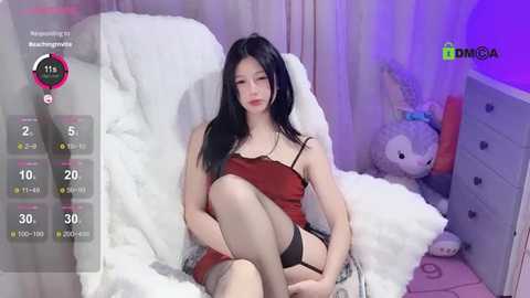 Media: Video of an East Asian woman with long black hair, wearing a red camisole, black garter belt, and stockings, sitting on a white fur chair, surrounded by plush toys.